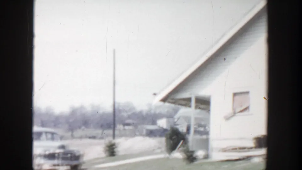 Grand Rapids 1956 frame with a house side, porch roofline, driveway area, utility pole, and a rounded mid-century car.