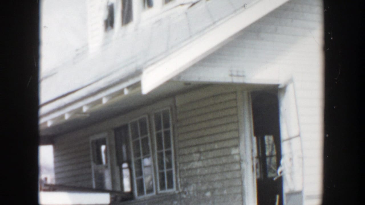 Two-story clapboard house exterior with porch, windows, and dark film borders.
