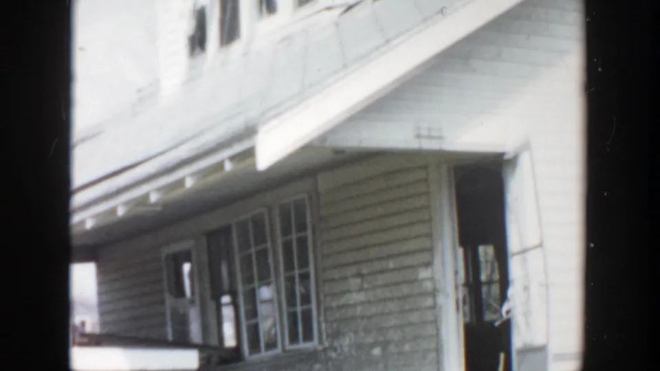 1956 Grand Rapids home-movie frame showing a two-story clapboard house with porch, window trim, and roof eaves.