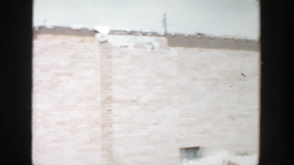 1956 Grand Rapids frame showing a light brick exterior, damaged roofline area, snow at the base, and a small basement window.
