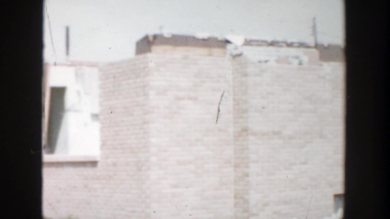 Pale brick building wall and window opening seen through dark vertical foreground framing.