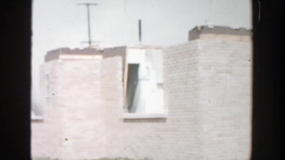 1956 Grand Rapids frame of an upper tan brick facade with an open window bay, roofline details, and dark foreground framing.