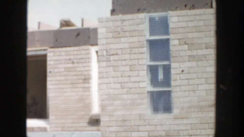 1956 Grand Rapids 8mm view of a brick facade with an open bay, a tall window with blue blinds, and visible film wear.