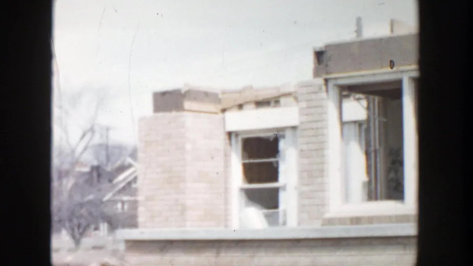 1956 Grand Rapids home-movie frame of damaged windows and roof edges on a neglected brick house.