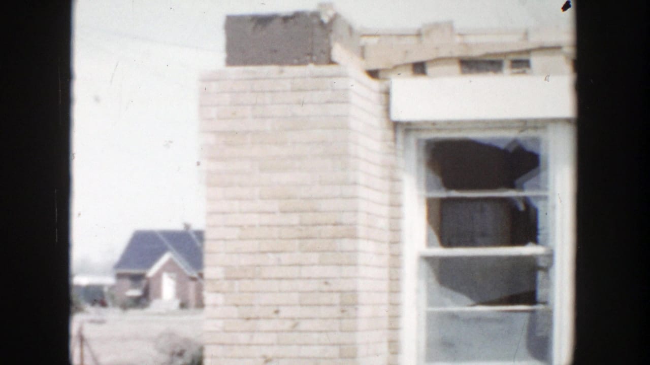 1956 Grand Rapids-area 8mm frame showing a damaged brick building with a broken window and small houses beyond.