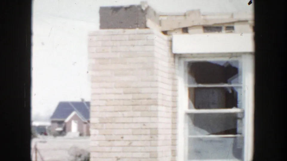 1956 Grand Rapids-area 8mm frame showing a damaged brick building with a broken window and small houses beyond.