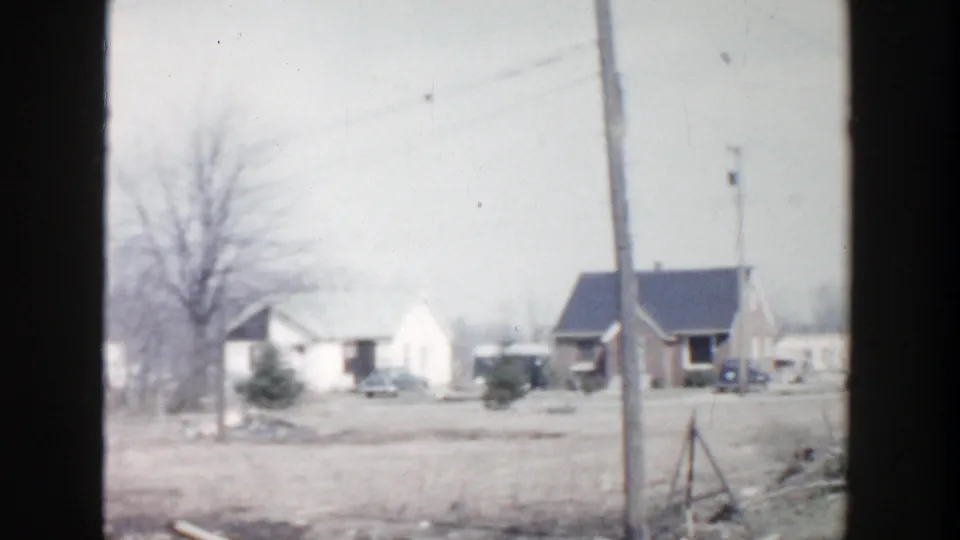 1956 Grand Rapids-area frame showing modest homes, utility poles, parked vehicles, bare trees, and winter ground in a rural residential scene.