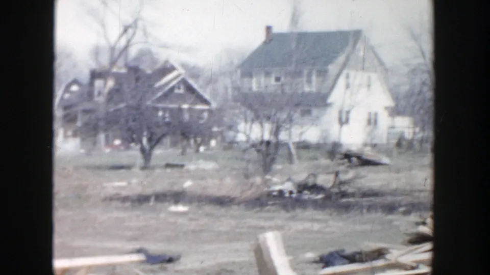 1956 Grand Rapids aftermath view of a house with visible structural damage beside another residence and scattered debris.