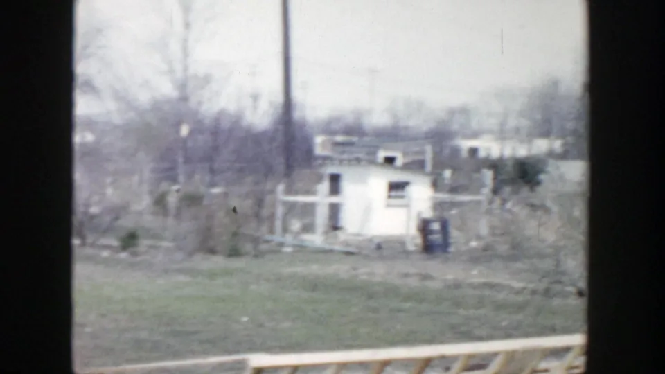 1956 Grand Rapids home-movie view of a small outbuilding, utility pole, open yard, and debris after damage.