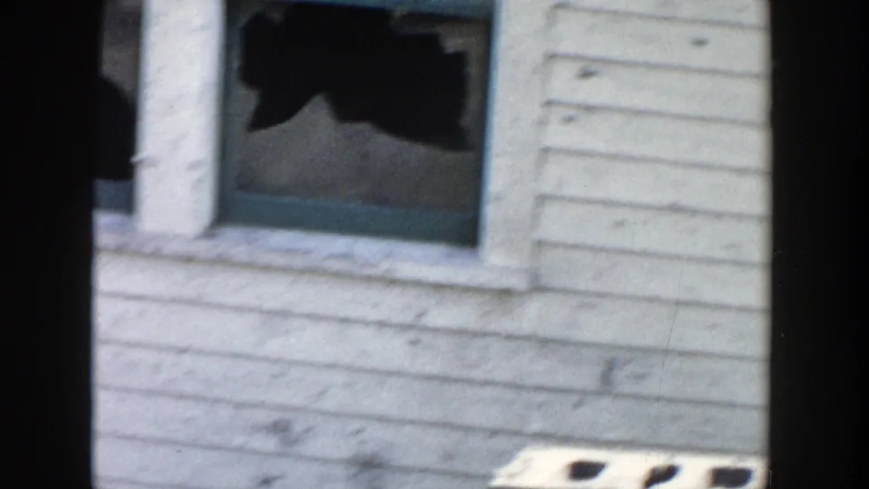 1956 Grand Rapids home-movie frame showing a close side view of the white clapboard house with a broken or open window.