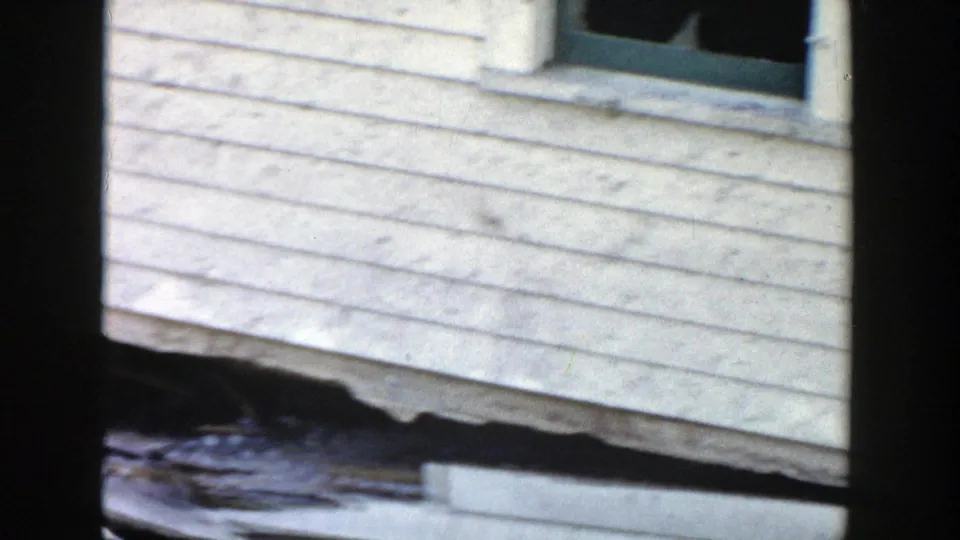 1956 Grand Rapids frame showing the house wall, window, and shadowed gap beneath the elevated structure near the foundation line.