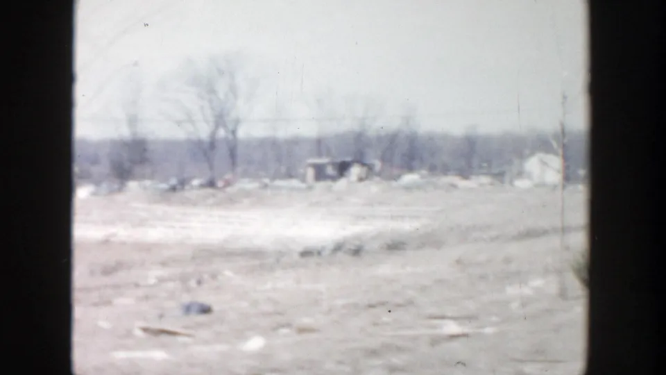 Snow-patched open ground with bare winter trees and distant structures in a 1956 Grand Rapids home-movie view.