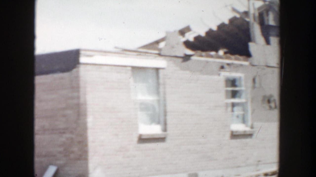 1956 Grand Rapids home-movie frame showing a brick house with exposed roof structure viewed through dark vertical framing.