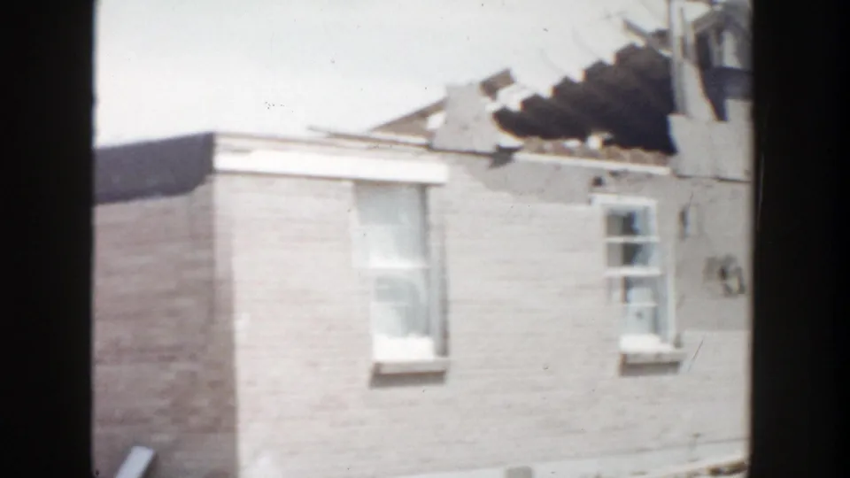 1956 Grand Rapids home-movie frame showing a brick house with exposed roof structure viewed through dark vertical framing.