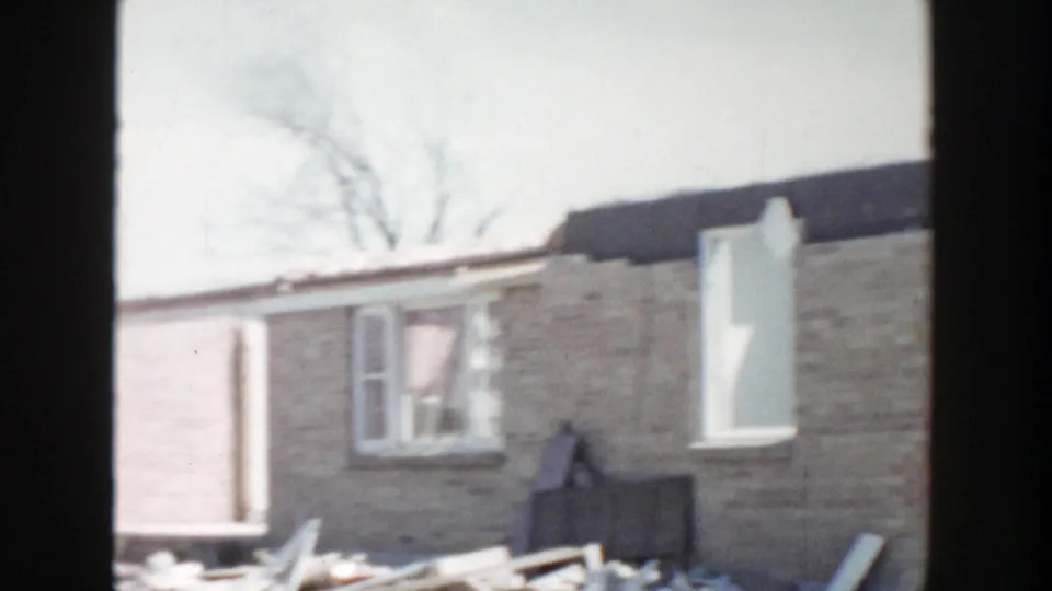 1956 Grand Rapids frame showing a partially altered brick house wall, open window area, and scattered renovation debris.