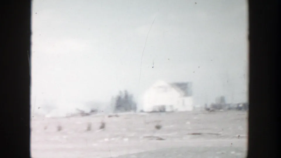 Soft 8mm view of a snowy Grand Rapids roadside with a white house, bare trees, and open ground near the road.