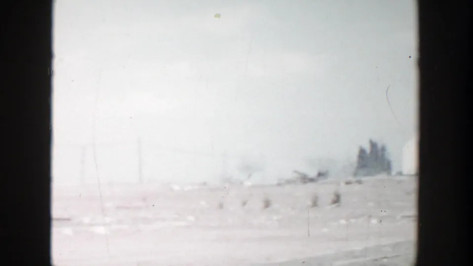 1956 Grand Rapids home-movie frame showing a hazy roadside landscape with utility poles and open ground before the car enters view.