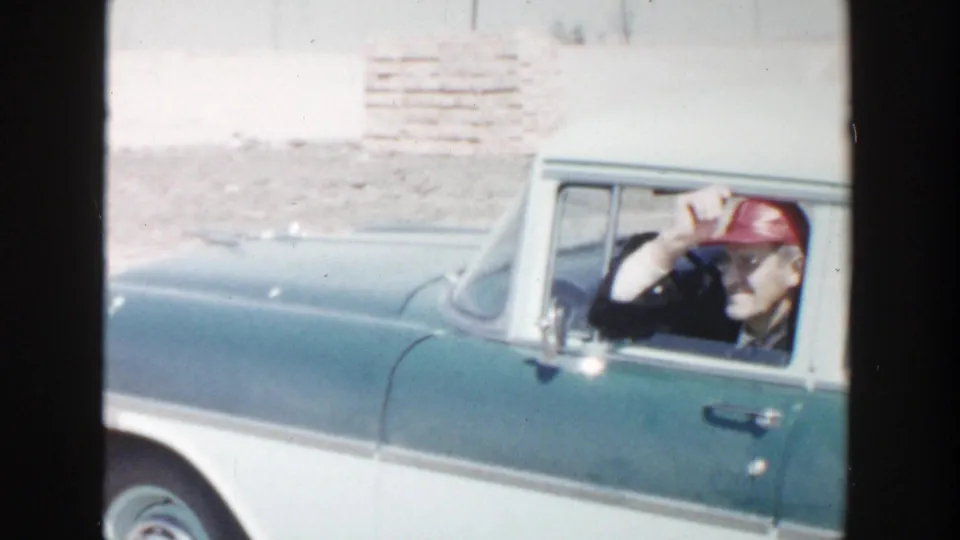 A man remains seated at the driver's window of a green and white station wagon in 1956 Grand Rapids home-movie footage.