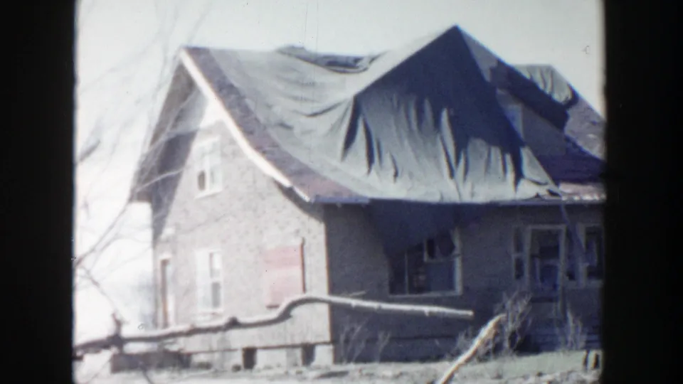 A brick house in Grand Rapids appears with a tarp covering roof damage and a fallen branch or limb across the yard.