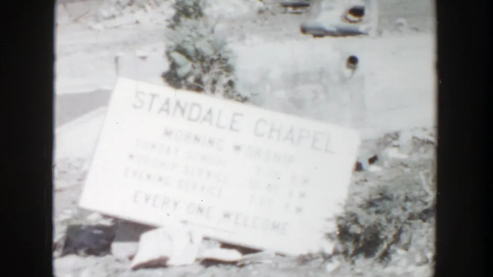 1956 Grand Rapids frame showing a fallen or tilted Standale Chapel sign with service information, debris, and shrubs around it.