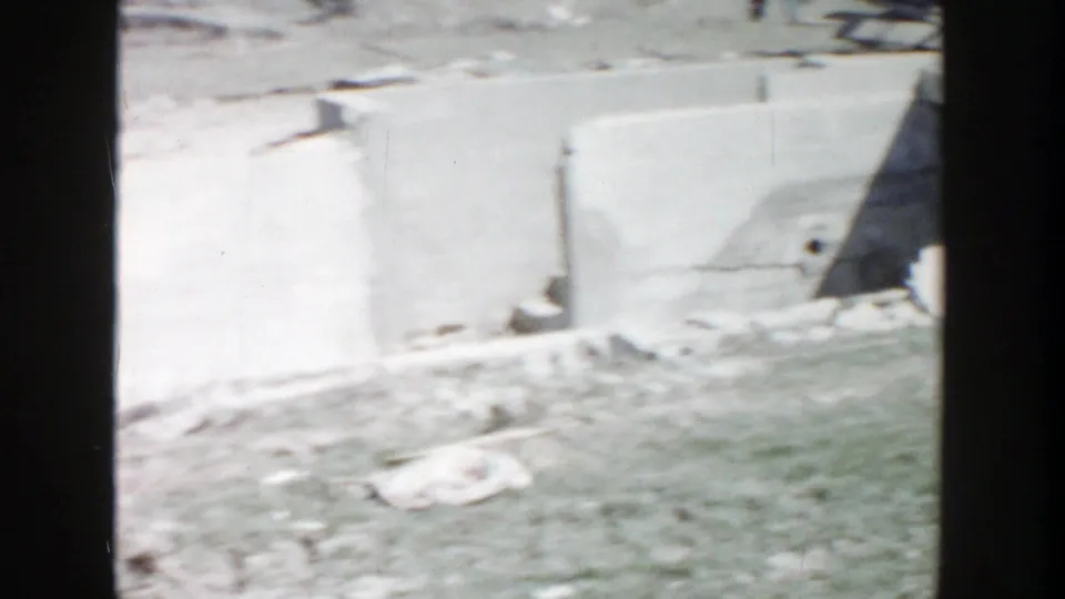 1956 Grand Rapids construction-site view with low concrete walls, loose materials, and open ground in soft 8mm focus.