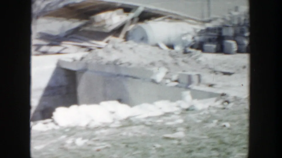 Outdoor work area in Grand Rapids with stacked blocks, rubble, containers, and partial concrete construction visible in 1956 footage.