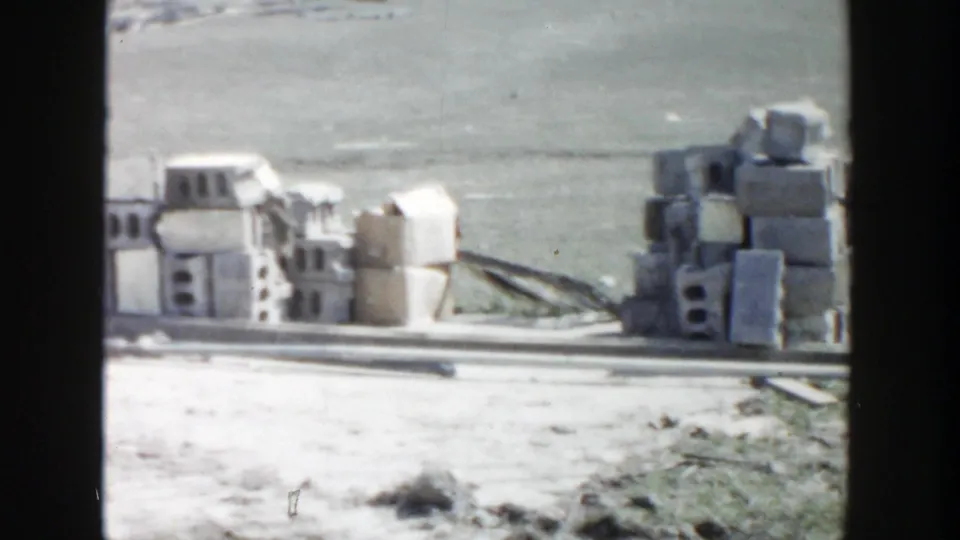 1956 Grand Rapids 8mm frame showing stacked concrete blocks, loose materials, and pale ground at a construction site.