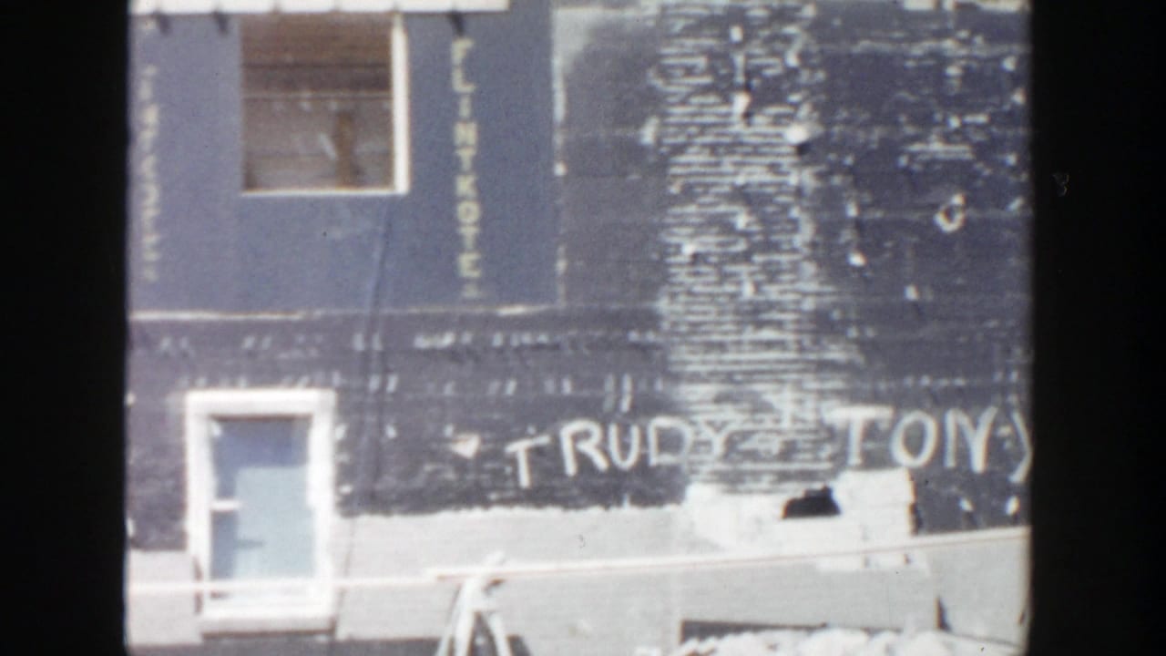 Blue-gray wall with doorway, white graffiti, and vertical sheathing lettering.