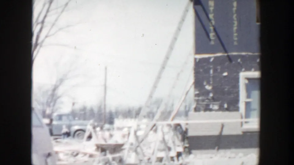 1956 Grand Rapids frame showing wood braces, a blue-gray wall section, construction debris, and a period car in the background.
