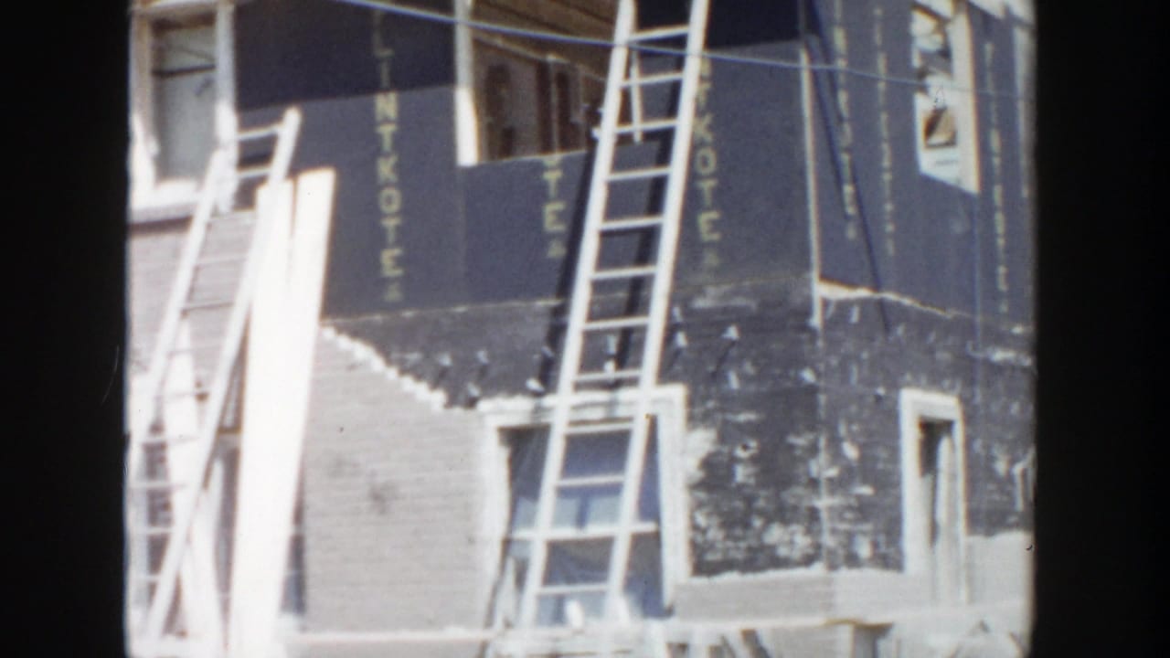 1956 Grand Rapids construction view showing a brick facade, leaning ladders, and black LINTKOTE sheathing panels.