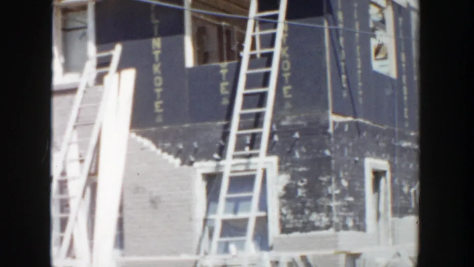 1956 Grand Rapids construction view showing a brick facade, leaning ladders, and black LINTKOTE sheathing panels.