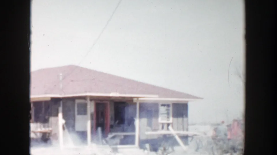 Grand Rapids 1956 home-movie frame showing a low single-story house exterior with porch posts, windows, and a red doorway area.
