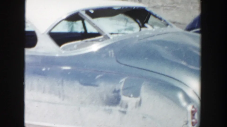 Close 1956 Grand Rapids home-movie view of a two-tone mid-century car, with its white roof and blue rear quarter filling the frame.