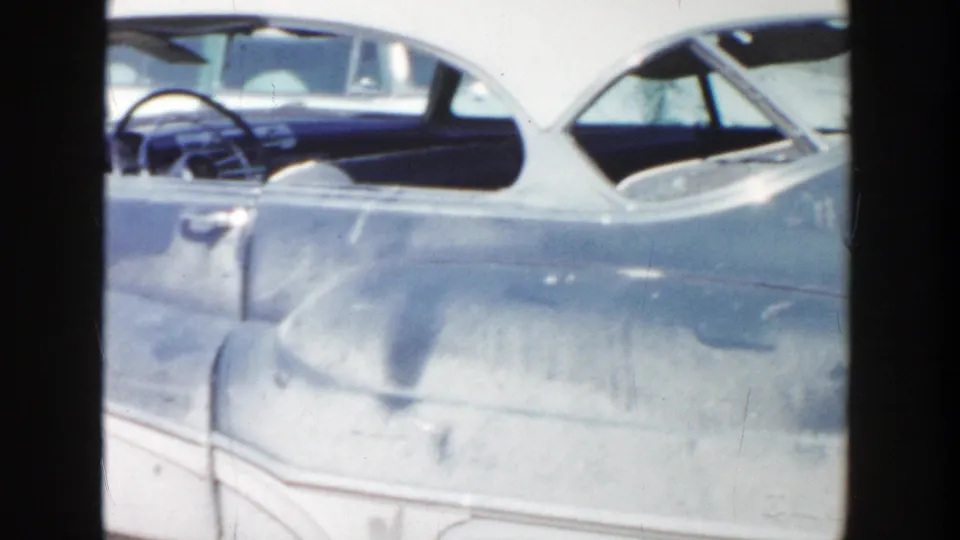 Grand Rapids 1956 frame showing the side of a two-tone 1950s car, with the steering wheel, windows, and rear bodywork visible.