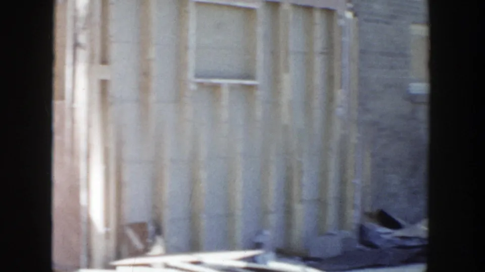 Grand Rapids 1956 home-movie frame showing damaged exterior wall framing, siding, debris, and dark film gate edges.
