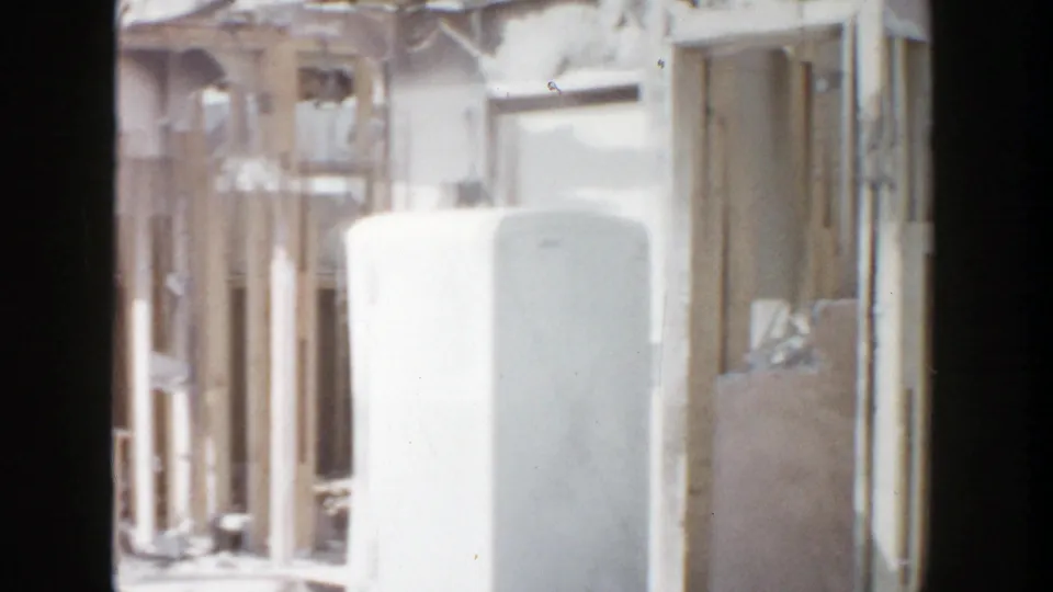 Grand Rapids 1956 storm aftermath frame with a white refrigerator amid exposed wooden studs and damaged walls.
