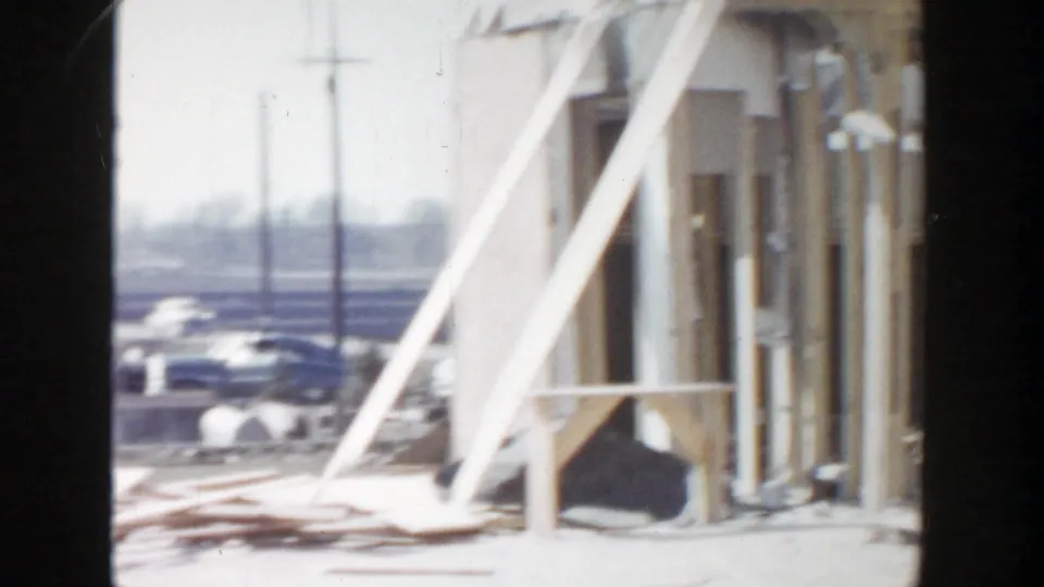 Grand Rapids 1956 frame showing a damaged building edge, diagonal supports, scattered lumber, and parked cars in the background.