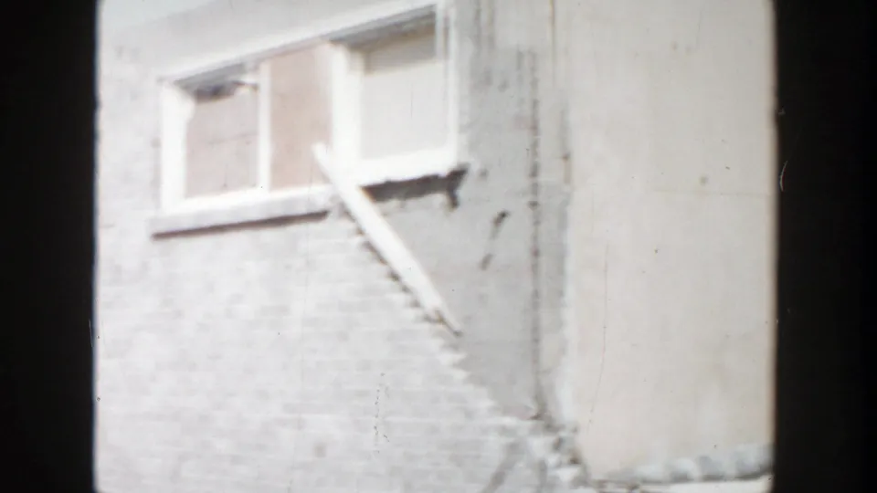 Grand Rapids construction frame showing a partly finished wall, window opening, diagonal board, and scattered material at ground level.
