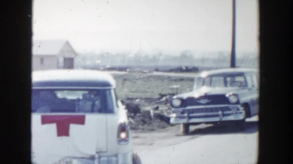 1956 Grand Rapids home-movie frame showing the rear of a white station wagon with a red marking as another classic car approaches on the rural road.