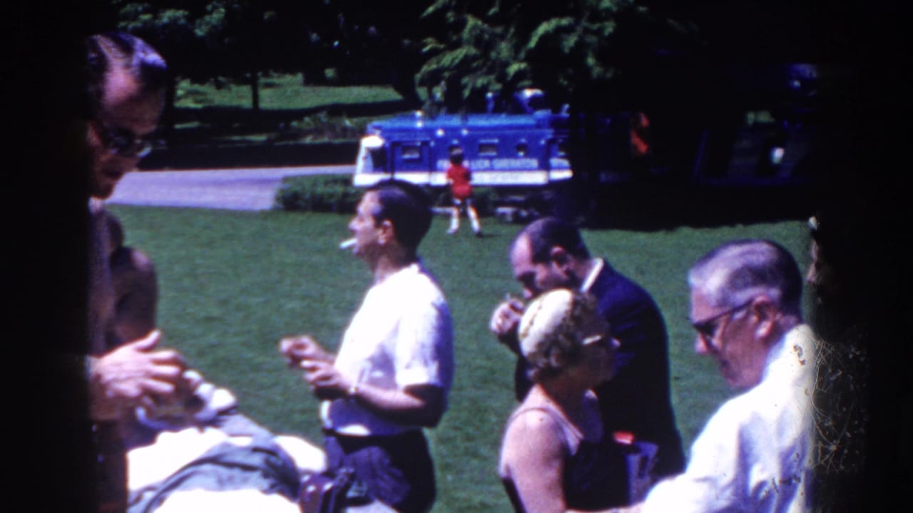 In 1958 French Lick, Indiana footage, adults in summer clothing gather on grass near a blue French Lick bus as men smoke.