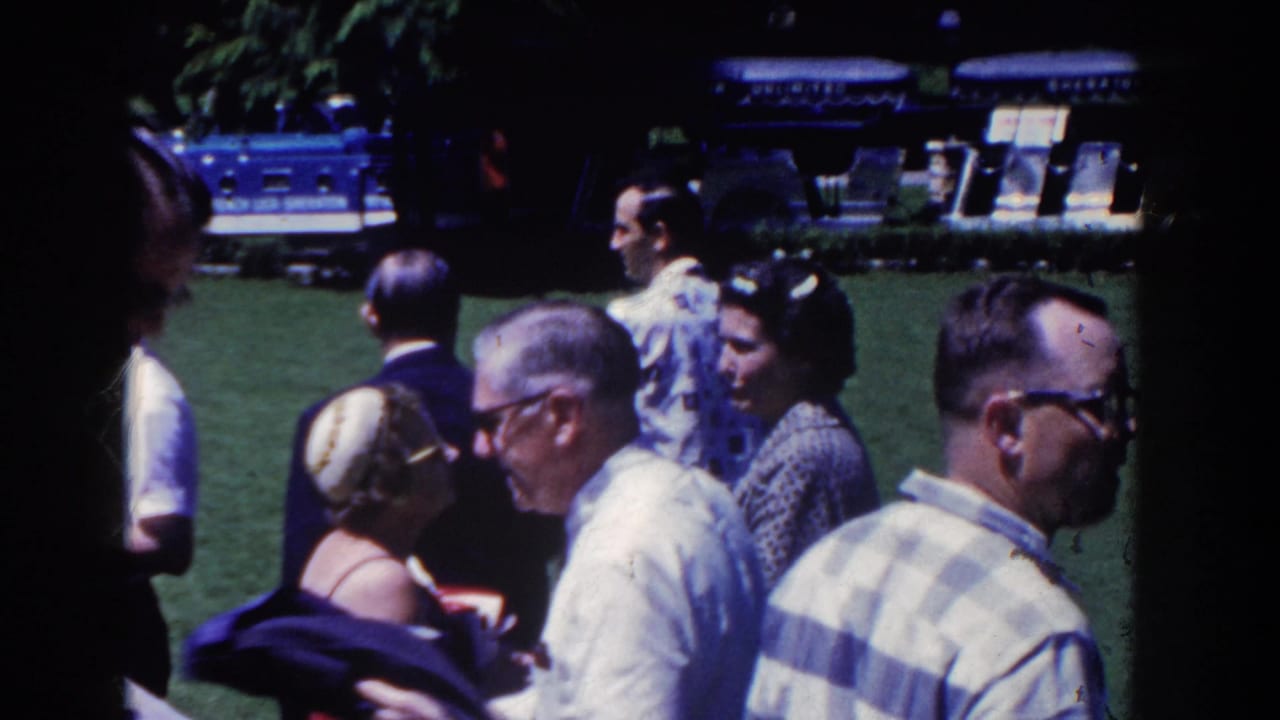 French Lick, Indiana home-movie frame from 1958 showing adults in period clothing gathered on a green lawn with shaded resort grounds behind them.