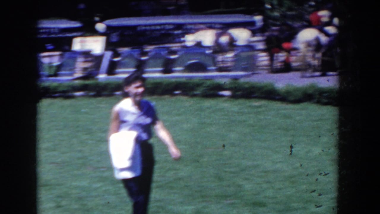 In 1958 French Lick, Indiana footage, a woman crosses a grassy resort area while guests and a carriage sign appear in the background.