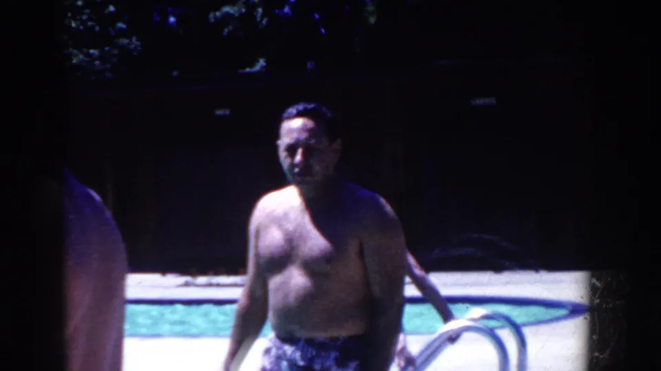 A shirtless man in swim trunks stands poolside in 1958 French Lick resort footage, filmed with dark shadows and soft 8mm color.