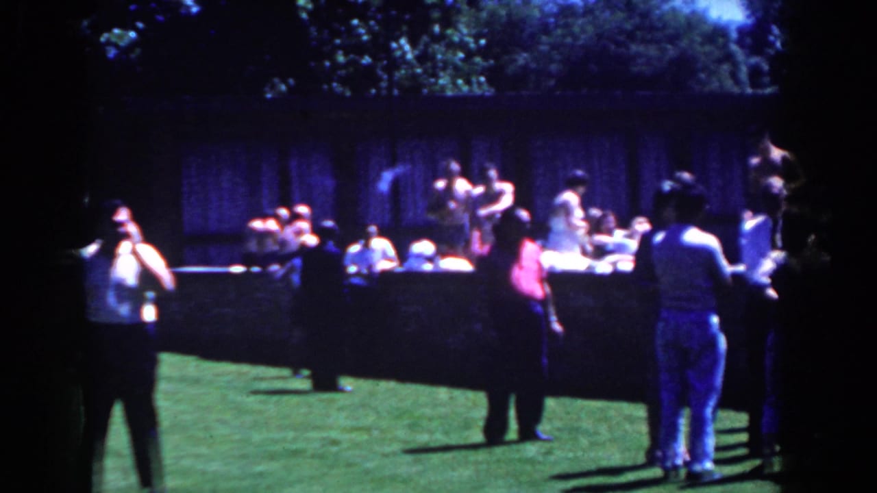 A group gathers on a grassy lawn in French Lick, Indiana, with people playing catch and spectators watching from behind a low wall.