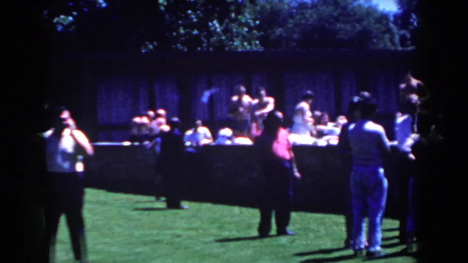 A group gathers on a grassy lawn in French Lick, Indiana, with people playing catch and spectators watching from behind a low wall.