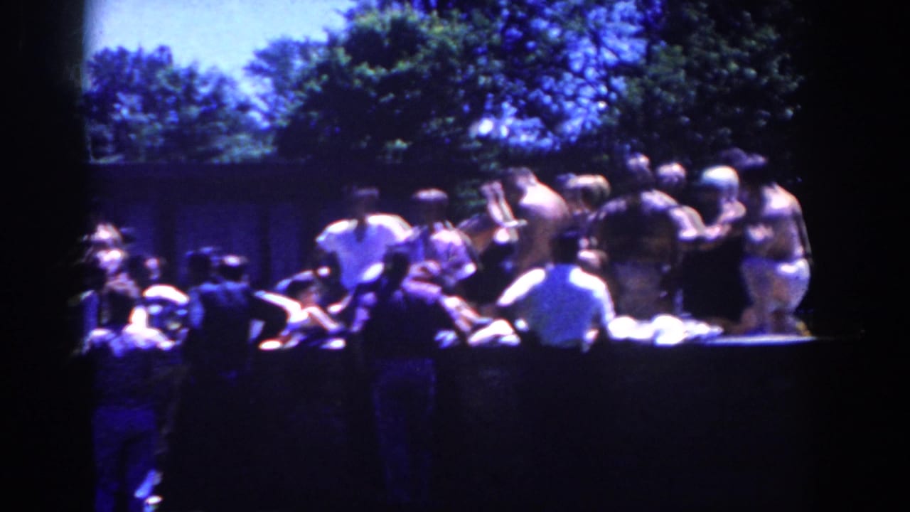 Men gathered around a long outdoor table in a shaded wooded area.