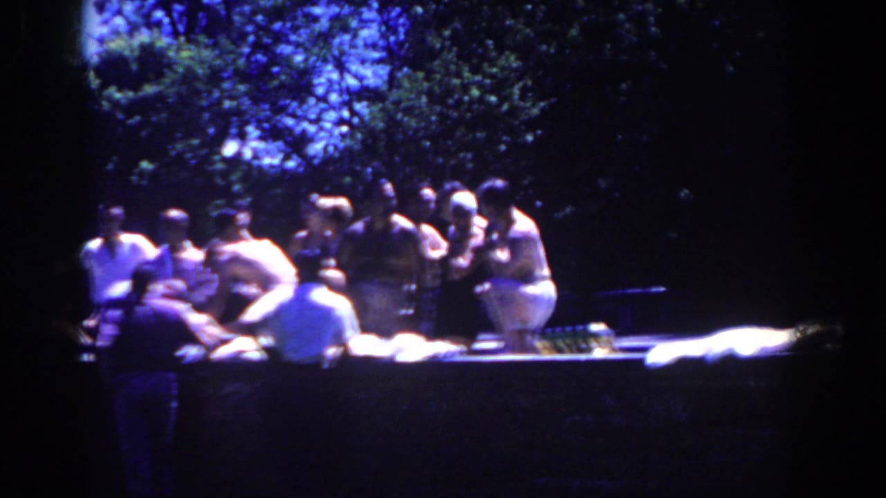Group of men standing and sitting near a long table under trees.