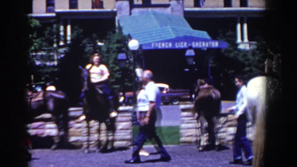 1958 French Lick street frame with riders and pedestrians moving past the French Lick-Sheraton awning.