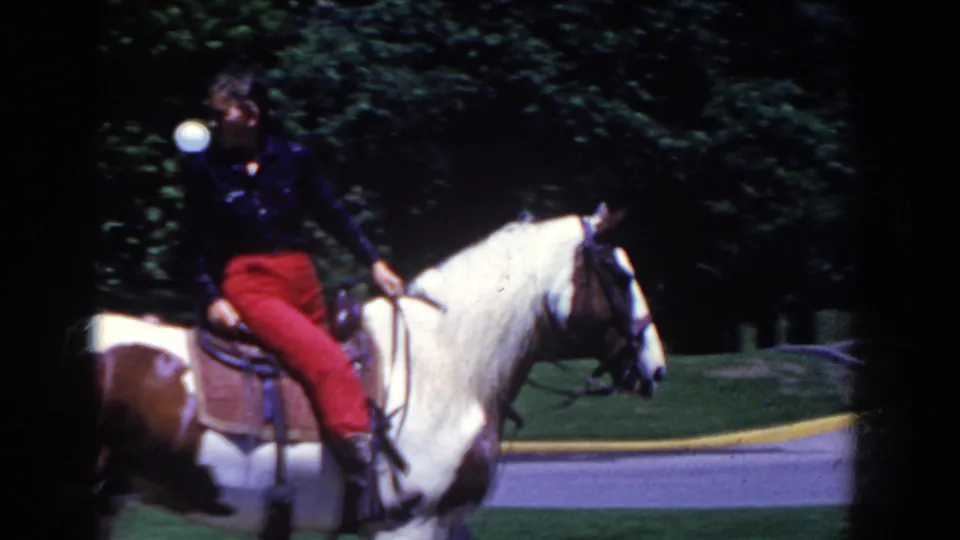 A rider in red pants sits on a white and brown pinto horse in French Lick, Indiana, with park greenery and road behind.