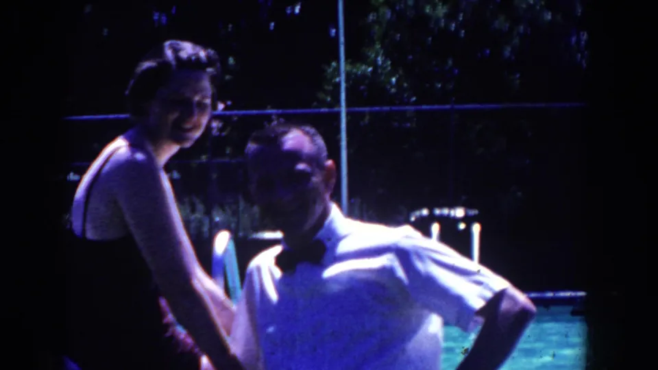 The couple remains seated at the pool edge in French Lick, with cool night lighting, fence lines, and trees visible behind them.
